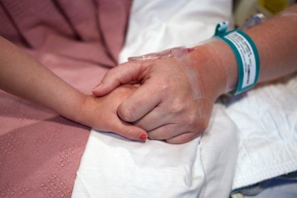 A woman in hospital bed holding a child's hand