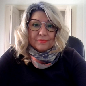 Smiling woman with shoulder length blond hair, olive skin and glasses.
