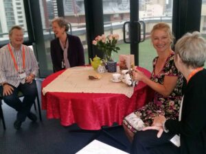 Foursmiling women sharing morning tea at a table with flowers and old fashioned teapots, cups and saucers.