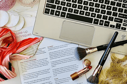 Information sheet, make-up tools, wig and scarf next to an open laptop on a desk.