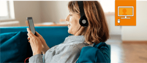 woman with headphones on sitting on coach and looking at phone.