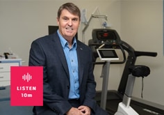 Robert Newton, researcher, wearing a navy suit and blue shirt, sitting casually in front of a treadmill. A red box overlays the image and says listen 10m.