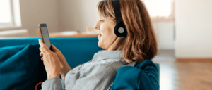 Image of woman from side profile wearing headphones and looking at phone on the couch