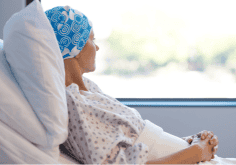 woman in headscarf sits in hospital bed looking out the window.