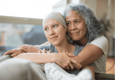 woman in headscarf sits with another woman showing support and care by having her arms around her shoulders.