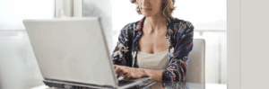 A woman sitting at a desk and looking thoughtful as she types on her laptop.