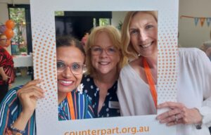 Three smiling women pose in a selfie frame with Counterpart's logo and website printed on it.