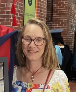 A woman with shoulder length dark blonde hair and fair skin, wearing glasses